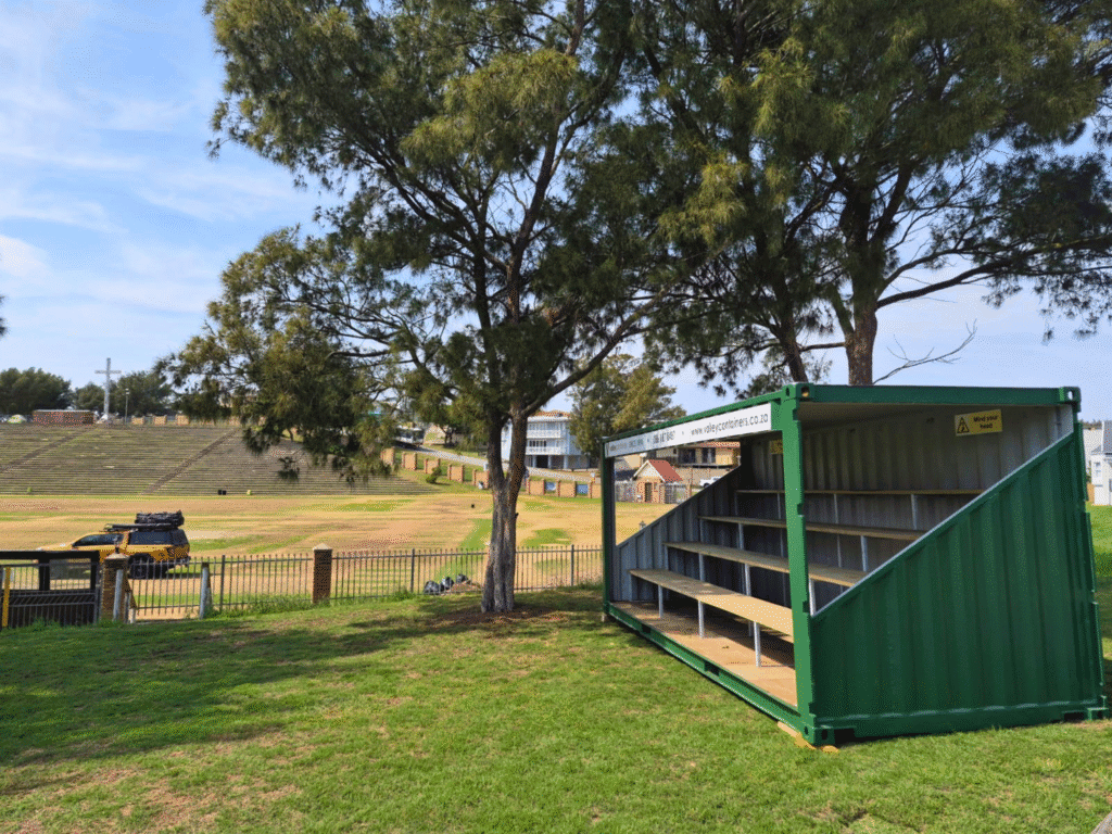 Container hire for events: green pavilion container with tiered wooden seating beside a sports field